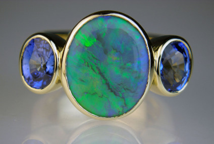 Black opal & sapphire ring in 18ct yellow gold - Spectacular ring in 18ct yellow gold set with 2.64ct cabochon black opal and flanked by a 2.05ct matched pair of Sri Lankan blue sapphires.