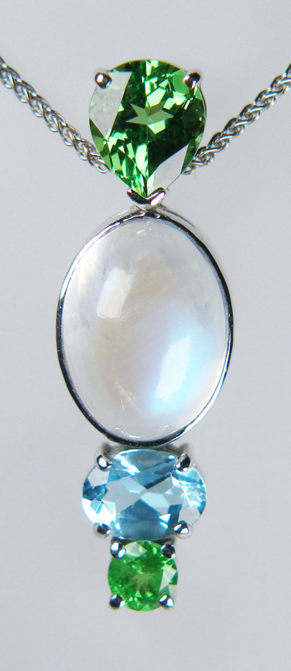 Birthstone pendant in 18ct white gold - Pendant consisting of a claw set 1.27ct pear cut tsavorite garnet, a rubover set 6.16ct oval cabochon moonstone, a claw set 0.87ct oval blue topaz and a claw set 0.25ct round tsavorite garnet. The pendant is made in 18ct white gold. The family birthdays are in January, June and November. 