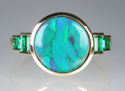 Black opal and emerald ring in 18ct yellow gold - Black opal from Lightning Ridge, New South Wales, Australia, weighing 1.95ct and measuring 11mm in diameter, set with 0.64ct of step cut emeralds, all gemstones rubover set and mounted in 18ct yellow gold ring.