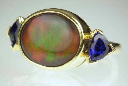 Black opal & sapphire ring - 5.64ct oval black Australian opal in red/green/gold colours set with  1.25ct matched pair of finest blue sapphires in 18ct yellow gold