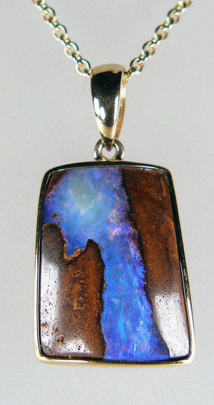Boulder opal pendant in 9ct yellow gold - Bright bluish purple boulder opal vein in banded ironstone set in a rubover 9ct yellow gold pendant. Pendant is 28mm long and 15mm wide. Chain is not included in the price.