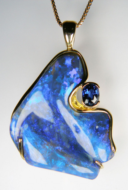 Black opal & sapphire pendant in 18ct yellow gold - Spectacular 49.17ct freeform carved black opal from Millionaires' Gully in the Glengarry Opal field near Lightning Ridge, mounted with a 1.5ct oval cushion cut natural blue sapphire and all mounted in 18ct yellow gold. The pendant measures 50 x 33mm and is suspended from an 18" 18ct yellow gold franco style chain. The chain is available for separate purchase.