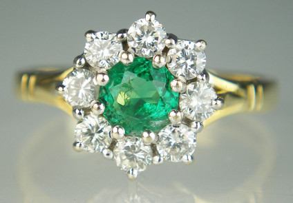 Emerald & diamond cluster ring in 18ct yellow gold - 0.34ct round cut emerald surrounded by 8 round brilliant cut diamonds totalling 0.48ct mounted in UK hallmarked 18ct white & yellow gold. This ring is pre-owned. It has been inspected by our gemmologist and goldsmith and has a six month warranty.
