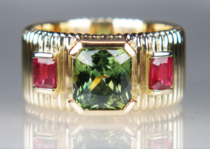 Sapphire ring in 18ct yellow gold - 2.34ct octagonal cut natural green sapphire of excellent clarity, rubover set and flanked by a 0.61ct pair of emerald cut natural rubies of excellent colour and clarity, all mounted in a finely ribbed 9mm wide ring band.