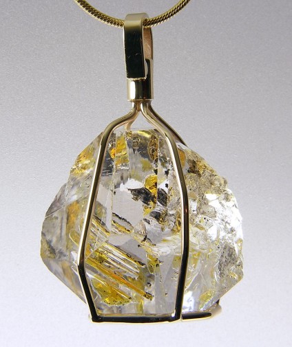 Oil included quartz pendant in gold - Pendant in 9ct yellow gold.  Rare oil included quartz crystals from Balochistan are set in individually handmade gold mounts.  The crystals are approximately 2-3cm in all dimensions and contain golden droplets of light oil, along with darker bitumen and an aqueous solution.  The inclusions fluoresce a strong bluish green under UV light.  Each pendant comes with a UV pen torch and an explanation of the crystal.  These crystals are extremely rare and it is difficult to find such perfect examples as sold by Just Gems.  The setting is precisely made to fit each unique crystal and has to be created without the application of heat, which could cause the crystal to fracture.  Each piece is handmade in Scotland and hallmarked in Edinburgh. Cufflinks and earrings also available.  A selection of crystals are available for bespoke designs.
