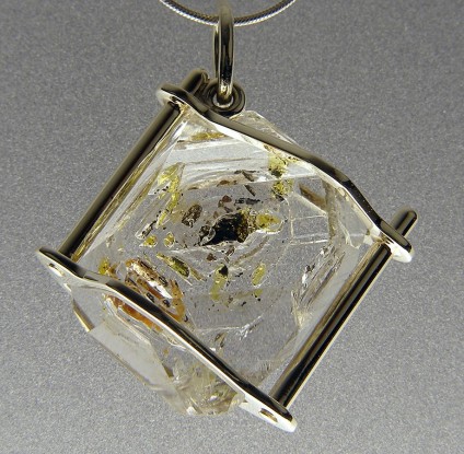 Oil included quartz pendant in gold - Oil included quartz crystal pendant set in 9ct white gold with chain.  Rare oil included quartz crystals from Balochistan are set in individually handmade white gold mounts.  The crystals are approximately 2-3cm in all dimensions and contain golden droplets of light oil, along with darker bitumen and an aqueous solution.  The inclusions fluoresce a strong bluish green under UV light.  Each pendant comes with a UV pen torch and an explanation of the crystal.  These crystals are extremely rare and it is difficult to find such perfect examples as sold by Just Gems.  The setting is precisely made to fit each unique crystal and has to be created without the application of heat, which could cause the crystal to fracture.  Each piece is handmade in Scotland and hallmarked in Edinburgh. Matching earrings are available. Also Cufflinks.  A selection of crystals are available for bespoke designs.
