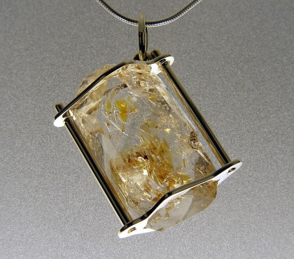 Oil included quartz pendant in gold - Oil included quartz crystal pendant set in 9ct white gold with chain.  Rare oil included quartz crystals from Balochistan are set in individually handmade white gold mounts.  The crystals are approximately 2-3cm in all dimensions and contain golden droplets of light oil, along with darker bitumen and an aqueous solution.  The inclusions fluoresce a strong bluish green under UV light.  Each pendant comes with a UV pen torch and an explanation of the crystal.  These crystals are extremely rare and it is difficult to find such perfect examples as sold by Just Gems.  The setting is precisely made to fit each unique crystal and has to be created without the application of heat, which could cause the crystal to fracture.  Each piece is handmade in Scotland and hallmarked in Edinburgh. Matching earrings are available. Also Cufflinks.  A selection of crystals are available for bespoke designs.
