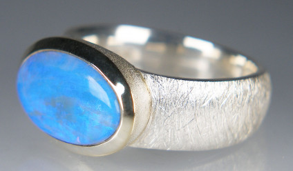 Crystal opal ring in silver - Pretty light blue translucent crystal opal oval, rubover set in silver ring. The bexel (rubover) is lightly gold plated. The opal is closed backed. The ring shank has a coarsely brushed texture. Opal is 15 x 8mm. Ring size is O1/2. This item is included in our 20th anniversary 50% sale and now costs £70.
