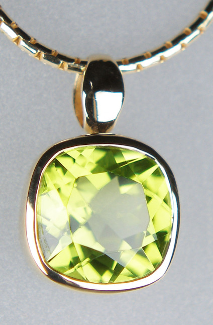 Cushion cut peridot pendant in 9ct yellow gold - Sparkling and vibrant cushion cut peridot pendant measuring 12 x 8mm rubover set in 9ct yellow gold. Price excludes chain.