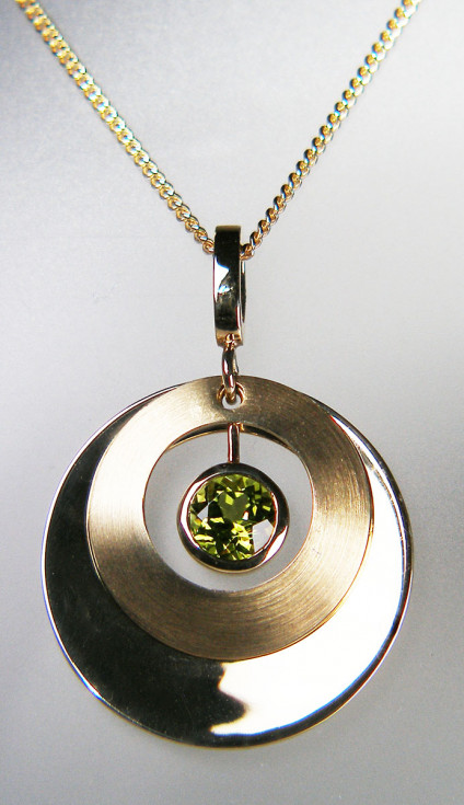 Peridot pendant in 14ct yellow gold - Beautiful and unusual pendant with moving disks of polished and satin finished yellow gold with sparkling 1.5ct round brilliant cut rubover set peridot. Pendant is 35mm long, 25mm wide and made from 14ct yellow gold. It is suspended from an 18", 18ct yellow gold chain. Pendant is £390, chain £320.