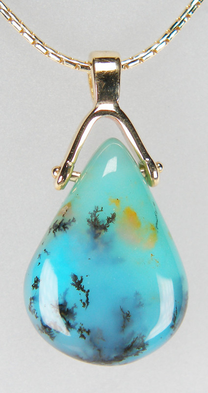 Peruvian opal drop pendant in 9ct yellow gold - Drilled drop shaped bead of attractive turquoise blue Peruvian opal with a delicate black dentritic lace pattern. The bead was hand carved and polished by US artisan company 'Out of Our Mines'. The opal is suspended from a 9ct yellow gold bail and measures 25 x 13mm. Price excludes the chain which is available separately.