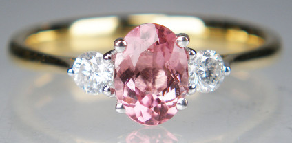 Pink tourmaline & diamond ring in 9ct yellow gold - Oval pink tourmaline weighing 0.74ct and flanked by two round brilliant cut diamonds weighing 12pt each (TDW 0.24ct), mounted in a dainty 9ct yellow gold ring