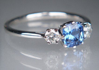 Sapphire & diamond ring in platinum - Dainty sapphire & diamond ring in platinum set with a 0.73ct cushion cut mid blue natural sapphire, flanked by a 0.24ct pair of G colour VS clarity round brilliant cut diamonds. The gems are all claw set in platinum. Ring size is N