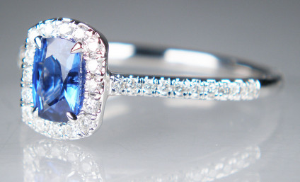 Sapphire & diamond ring in 9ct white gold - Cushion cut blue sapphire with diamond halo and diamond set shoulders in 9ct white gold. Sapphire weighs 0..65ct and there is a total diamond weight of 0.22ct. Ring size is N.