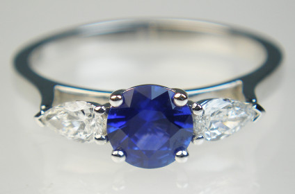 Sapphire & pear cut diamond ring in 18ct white gold - Round cut 0.78ct blue sapphire (5.9mm in diameter), set with a 0.33ct pair of pear cut diamonds in 18ct white gold. The ring is designed to fit next to a wedding band and is size J. All our jewellery can be sized to fit your finger by our expert goldsmiths.