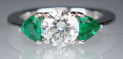 Diamond & emerald ring in 18ct white gold - 1.30ct round brilliant cut diamond in J colour SI2 clarity, claw set and flanked by a 0.47ct matched pair of fine trillion cut emeralds. Ring is made in 18ct white gold. Ring size M 1/2