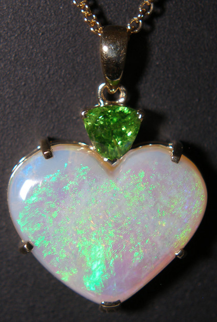 Opal & green garnet pendant in 9ct yellow gold - Dainty pendant with claw set heart cut crystal opal from Lightning Ridge, Australia weighing 5.13ct topset with a trillion cut green tsavorite garnet weighing 0.38ct, all mounted in 9ct yellow gold. The pendant measures 23x17mm. The chain is available for separate purchase.